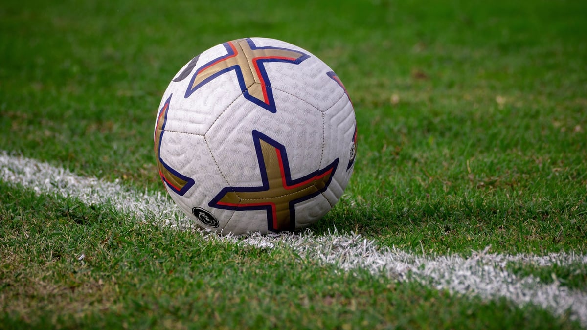 Fotboll med färgglada detaljer placerad på sidlinjen på en välklippt gräsplan, med 1X2-logotyp i hörnet.