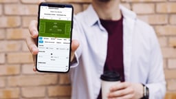 En person håller upp en telefon med pre-match-betting hos 1X2.