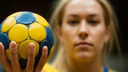 En svensk handbollsspelare lyfter upp en handboll mot kameran.